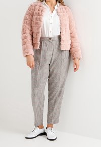 Giacca in pelliccia sintetica rosa con design trapuntato, abbinata a pantaloni a vita alta a quadretti e scarpe bianche con lacci.