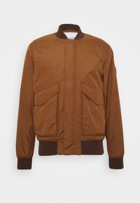 Brun bomberjacka med ståkrage, zip-förslutning, två framfickor, ribbad manschett och nederkant. Slät textur med matt finish.