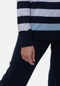 Långärmad randig topp med horisontella band i marinblått, ljusblått och vitt, tillsammans med mörk marinblå tajta byxor. Mjuk tyg, avslappnad passform.