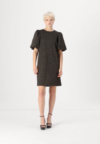 Vestido preto texturizado com mangas bufantes, até aos joelhos, apresentando um decote redondo e uma silhueta reta. Combinado com saltos altos pretos.