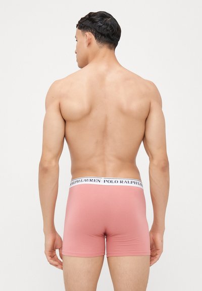 Svetlo roza bokserice iz gladkega materiala z belim pasom, na katerem je črn napis "POLO RALPH LAUREN."