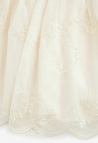 Tissu en tulle ivoire clair avec broderie blanche complexe de fleurs et de papillons. Détail d'ourlet festonné avec une texture douce. Aspect plus doux et superposé.