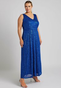 Blå paljettmaxiklänning med V-ringning, ärmlös design och en figursydd midja, som leder ner till en hel längd kjol. Silverfärgade högklackade sandaler.