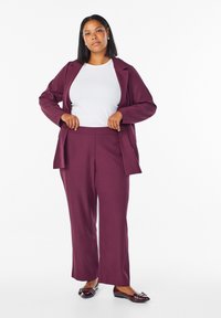 Chaqueta de traje a medida color burdeos y pantalones de pierna ancha sobre una blusa blanca. Bailarinas con detalle de lazo. Tejido suave y diseño estructurado.