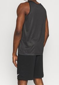 Uomo visto da dietro che indossa una canottiera nera senza maniche e pantaloni corti neri con un piccolo logo bianco sulla gamba sinistra.