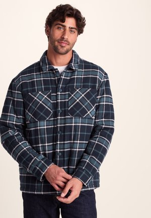 Flannel shirt featuring a dark navy and teal plaid pattern, long sleeves, two front pockets, and button closures. Soft fabric texture.