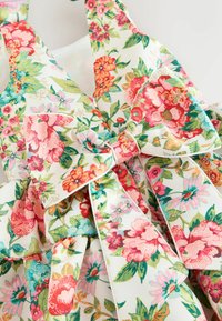 Cvetlična obleka z rožami v roza, rdeči in modri barvi ter zelenimi listi, z velikim trakom, zavezanim okoli pasu, na belem ozadju.