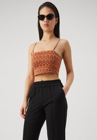 Orange cropped top with wave pattern, spaghetti straps, textured fabric. Paired with loose-fitting black pants with elastic waistband.