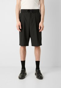 Mustat, polven mittaiset shortsit, jotka on valmistettu sileästä, joustavasta materiaalista. Niissä on joustava vyötärönauha ja kiristysnaru. Yhdistetty mustien sukkien ja kenkien kanssa.