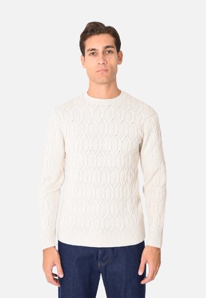 Maglione lavorato a maglia crema con un motivo esagonale, scollatura rotonda e polsini a coste, abbinato a jeans in denim blu scuro.