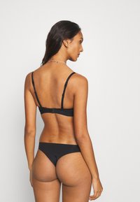 Ensemble de lingerie noire comprenant un soutien-gorge simple et lisse avec des fines bretelles et un string assorti, tous deux fabriqués en tissu doux et extensible.