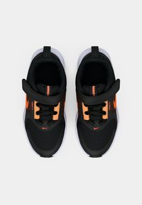 Μαύρα αθλητικά παπούτσια με πορτοκαλί λεπτομέρειες, υφή στο άνω μέρος, κλείσιμο με κορδόνια και ιμάντα με αυτοκόλλητο, σε λευκή σόλα. Άποψη από πάνω.