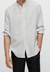 Chemise légère à manches longues en tissu blanc avec des rayures verticales bleu marine, devant boutonné et col montant. Manches retroussées.