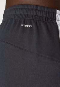 Primer plano de una persona que lleva pantalones cortos deportivos negros con una cintura elástica y el texto "BEE COOL" cerca de la cintura.
