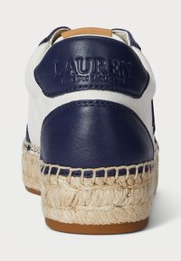 Baltas kanvas kedas ar tumši zilu ādas akcentu, pīti jutu vidusdaļa un brūns papēža cilnis. Ir iegravēts zīmola logo uz papēža.