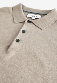 Polo shirt bej dintr-un material tricotat, cu un guler clasic, trei butoane negre și un detaliu cu dungi în interiorul gulerului.