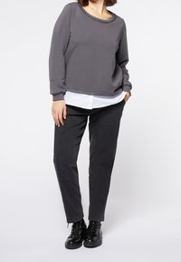 Sudadera gris con escote adornado con cuentas, combinada con una camisa blanca. Se acompaña de pantalones negros ajustados y botas negras con cordones.