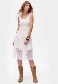 Robes midi en dentelle blanche avec un corps ajusté et une jupe évasée. Elle présente un haut en tricot texturé et un ourlet à volants, associée à des bottes de cowboy couleur beige.