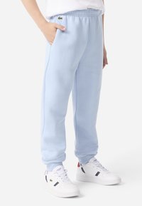 Svetlomodré teplákové nohavice z fleecu s elastickým pásom, bočnými vreckami a vyšívaným logom, v kombinácii s bielymi teniskami s námorníckymi detailmi.
