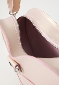 Lys rosa lærveske med sølvglidelås, synlige sømmer og en glatt innside med en mørkere rosa fôr. Kompakt design.