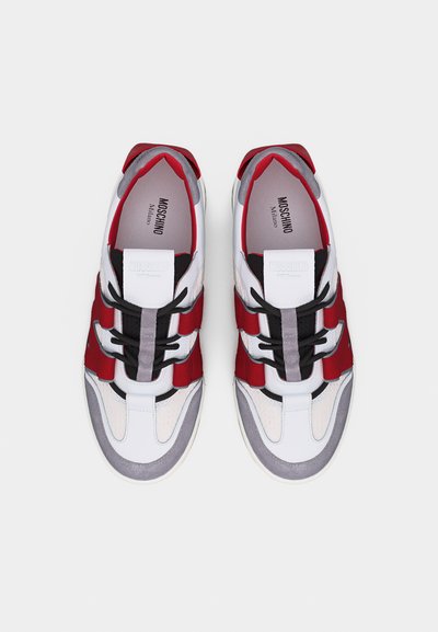 Ζευγάρι λευκά, κόκκινα, γκρι και μαύρα αθλητικά παπούτσια Moschino Milano με μαύρα κορδόνια, ορατά από πάνω, σε λευκό φόντο.
