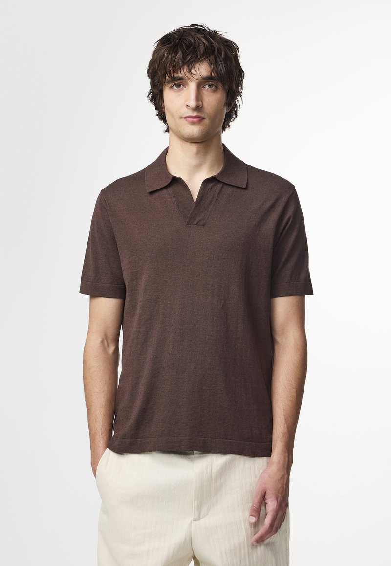 Polo shirt marron à manches courtes avec un col et une coupe décontractée. Le tissu semble doux et texturé, agrémenté de lignes simples et épurées.
