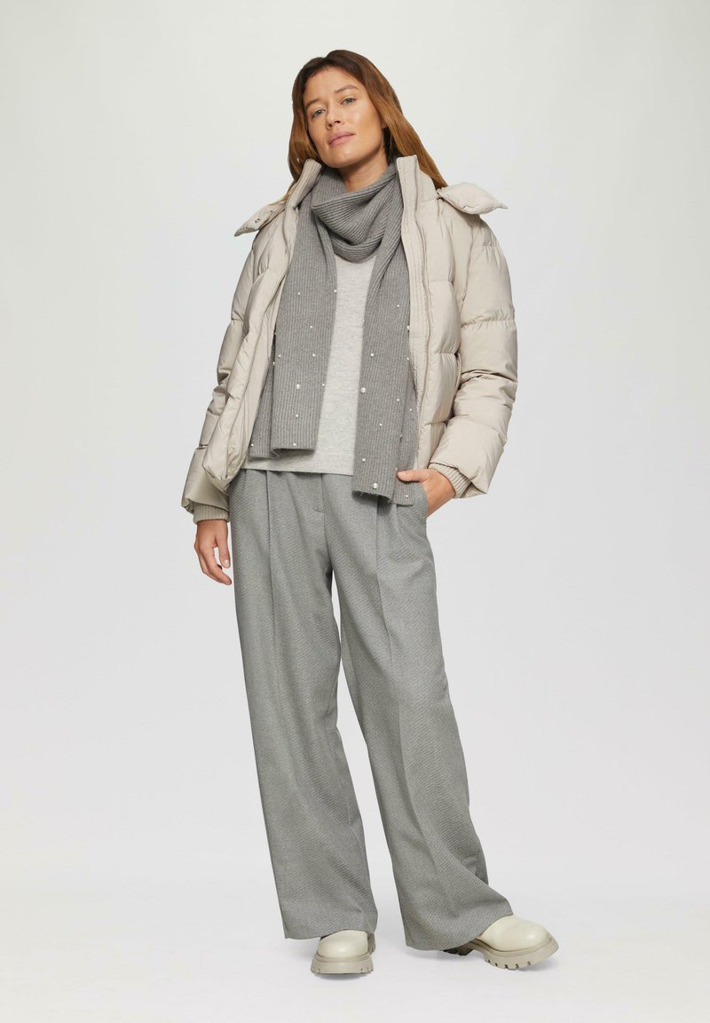 Veste matelassée beige clair avec un col haut, pull gris à texture côtelée, pantalon gris à jambes larges et écharpe grise avec des accents subtils.