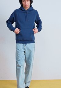 Navy blue cotton hoodie with a front pocket, drawstring hood, and ribbed cuffs, paired with light blue straight-leg jeans and black sneakers.