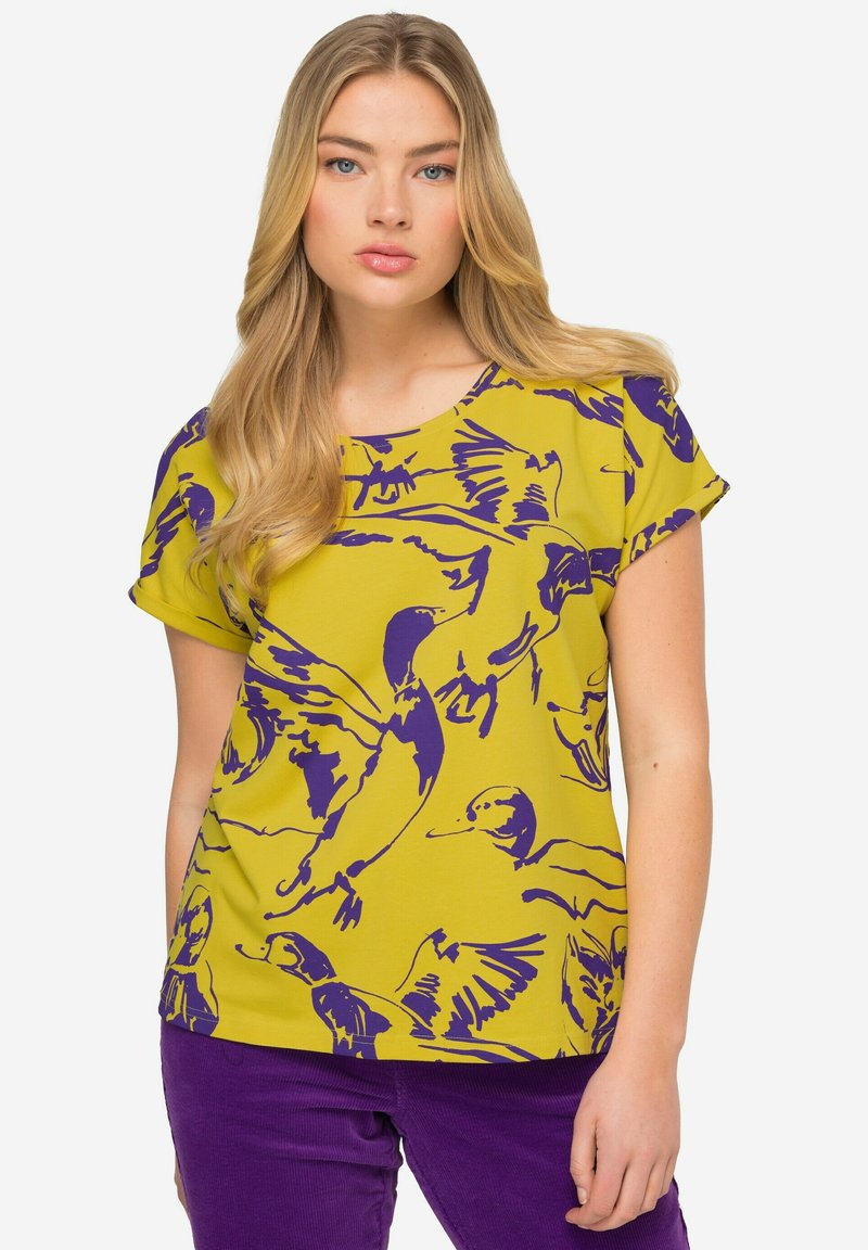 Camisa de manga corta en amarillo brillante con un estampado de pato púrpura. La tela tiene una textura suave y un corte relajado y holgado.