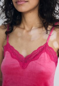 Fuchsia satijnen camisole met kantafwerking langs de halslijn. Dunne verstelbare straps en een zachte textuur. Heeft een V-hals vorm.