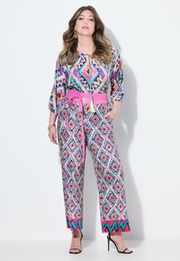 Flerfärgad jumpsuit med geometriska mönster, med ett rosa bälte, korta ärmar och vida ben. Slät tyg med en glänsande yta.