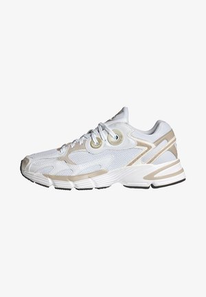 White athletic shoe with beige accents, mesh upper, and rubber sole. Features rounded toe, laces, and distinctive side detailing.