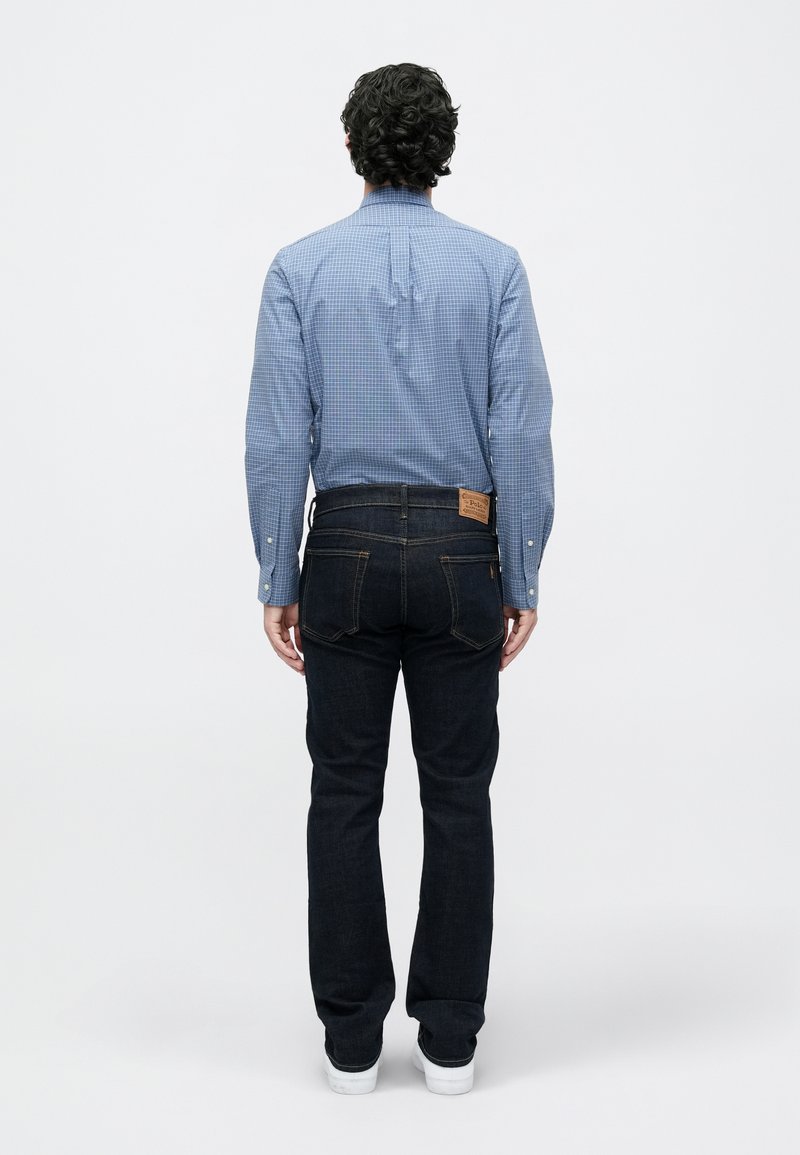 Blåternet knap-op skjorte med lange ærmer, parret med mørke denim jeans og hvide sneakers, set fra ryggen.