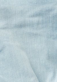 Tissu en denim bleu clair avec un tissage diagonal visible et des plis créant des ombres douces et une texture.