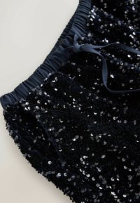 Black sequin shorts with a gathered waistband and satin ribbon tie. Features a soft texture and shiny, circular sequin pattern throughout.