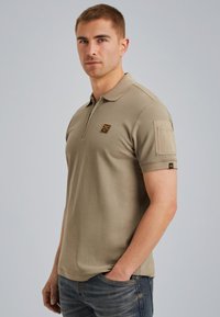 Beige poloshirt van een katoenmix met een klassieke kraag, korte mouwen en een borstpatch met een logo. Standaard pasvorm, gecombineerd met jeans.