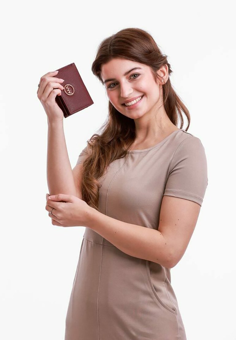 Burgundy leather wallet with a textured finish, featuring a logo accent. Held by a person wearing a beige dress, with a plain background.