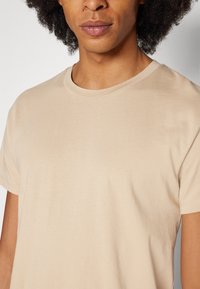 Beige katoenen T-shirt met een ronde hals en korte mouwen, met een gladde, egale textuur en een minimalistisch design.