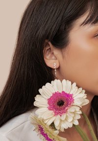 Orecchini a catena d'argento con gemme trasparenti, caratterizzati da un design floreale. In primo piano, grandi margherite gerbera bianche con accenti rosa.