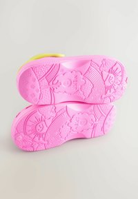 Heldere roze rubberen zolen met textuurpatronen, waaronder bloemen en zonontwerpen, en een gele band voor een veilige pasvorm.