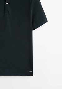 Polo noir à manches courtes, fabriqué en tissu texturé. Comprend une patte de boutonnage à deux boutons et un petit logo sur l'ourlet.