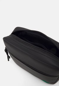 Schwarze Kulturtasche aus strukturiertem Material mit einem oberen Reißverschluss, die ein sauberes Innenleben und ein kleines grünes Akzentdetail aufweist.