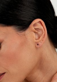 Roségoldene Ohrstecker mit bunten Edelsteinen, die ein florales Design und eine polierte Oberfläche aufweisen, getragen am Ohrläppchen.