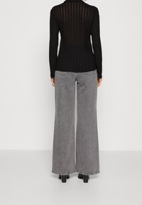 Czarny prążkowany longsleeve z odkrytymi plecami, zestawiony z szarymi dżinsami o wysokim stanie i szerokich nogawkach. Oba elementy charakteryzują się teksturowanym wykończeniem.