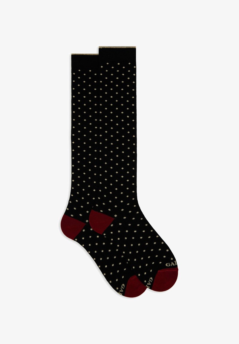 Schwarze knielange Socken mit kleinen beigen Punkten und dunklen roten Fersen- und Zehenakzenten, flach nebeneinander ausgelegt.