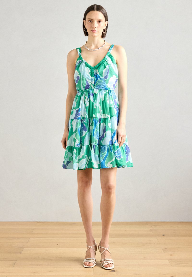 Robe verte à imprimé floral avec un design en niveaux. Caractérisée par des bretelles fines, un col en V et une taille ajustée. Complétée par des sandales légères à lanières.