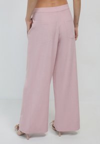 Helle rosa, weite Hose mit glatter Textur. Sie verfügt über Gesäßtaschen und einen hohen Bund, kombiniert mit nude-farbenen Absatzschuhen.
