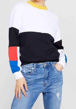 Sweatshirt avec des blocs de couleur jaune, noir, rouge et bleu. Fabriqué en tissu doux, il présente une coupe décontractée et des manches longues. Assorti à un jean clair.
