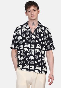 Camicia a maniche corte bianco e nera con motivi astratti di foglie e geometrici, in tessuto leggero, con bottone anteriore e vestibilità rilassata.