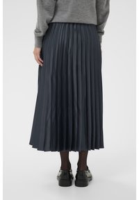 Gonna midi plissè di un blu navy scuro realizzata in un tessuto liscio e lucido. Presenta una vita alta e arriva sotto i polpacci, abbinata a scarpe nere.